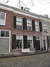 Pand met aan de achterzijde een gepleisterde puntgevel en aan de voorzijde een eenvoudige gevel onder kroonlijst met gesneden klossen en rozetten