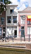 Pand met tot ingezwenkte gevel met lijst veranderde trapgevel, waarvan de zijafdekplaten onderaan nog bewaard zijn. Gevel gesausd, ramen en pui modern. Gevelsteen, met cartouche en engelenkopje