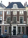 Pand met Ionische pilastergevel. Bakstenen gevel met zandsteenbanden rechte kroonlijst met gebeeldhouwde festoenen. Stoephek met palen en kettingen
