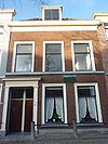 Pand met brede bakstenen gevel. Ingangspartij met omlijsting. Hardstenen stoep met stoeppalen