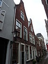 Pand met verdieping onder zadeldak met halsgevel waarin ongedeelde- en 6-ruitsschuifvensters in geprofileerde omlijstingen; 9-ruitsschuifvenster in top