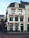 Pand met gepleisterde gevel met rechte kroonlijst, vensters met ronde hoeken. Mansarde dak. Stoeppalen en staaf