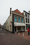Hoekpand met bakstenen gevel met rechte kroonlijst. Schilddak. Onderpui gewijzigd