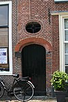 Poortje. Geprofileerd gemetseld rondboogpoortje van geslepen steen. Boven poortje ovaal venster met smeedwerk
