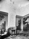 Interieur woonkamer met stucplafond, geschilderde behangsels en schouw met kachel - Leiden - 20136252 - RCE -  Stucplafond/ Behangsel: Interieur woonkamer met stucplafond, geschilderde behangsels en schouw met kachel 