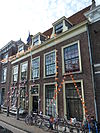 Pand met brede gevel met rechte kroonlijst. Hoog zadeldak in topgevels aan weerszijde uitlopend