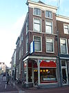 Hoekpand uit de gewijzigde voorgevel onder rechte kroonlijst, sierankers. Winkelpui met ijzeren versieringen in Art-Nouveau
