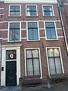 Pand met bakstenen gevel met rechte kroonlijst, deuromlijsting Lod. XV op metselwerk van verdieping resten van geverfde banden. Hardstenen stoep met palen