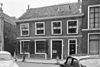 Laag huis met rechte kroonlijst, beneden intact, hier enige schuiframen met oude roeden en luiken. Stoep met palen