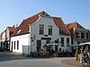 Hoekpand, in oorsprong boerderij met links een gezwenkte topgevel, afgedekt door een rechte lijst en rechts een opkam