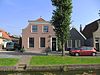 Pand met afgewolfd zadeldak en ingezwenkte gevel onder rechte lijst waarin gesneden deur
