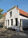 Pand onder zadeldak, dat aan de voorzijde is afgewolfd en met gepleisterde, ingezwenkte gevel onder lijst