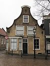 Hoekpand met in- en uitzwenkende topgevel, voorzien van natuurstenen hoekvoluten en een geprofileerde afdekking