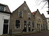 Pand, met zadeldak en puntgevel, waarin vlechtingen. Twee deuren met geprofileerde kalven en eenvoudige bovenlichten