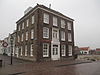 Markant gelegen monumentaal huis met twee verdiepingen en een omlopend schilddak. Vensters met geprofileerde dorpels en, in de voorgevel, een eenvoudige omlijsting van de ingang met het bovenvenster