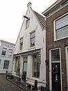 Hoekpand onder hoog zadeldak met aan voor- en achterzijde puntgevels, waarvan de voorste een kleine frontonbekroning heeft. Stoeppaal op de linkerhoek