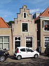 Huis met trapgevel met geprofileerde dekplaten en gewijzigde topafdekking. Ontlastingsbogen van vroegere vensters. Topanker