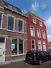Hoog pand met rood gesausde gevel, waarvan de zijkanten zijn afgeschuind