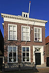 Pand in de rechter zijmuur, ter breedte van drie vensterassen en bestaande uit begane-grond en verdieping. Gesneden deuren en gesneden bovenlicht in late Lod. XVI-vormen, geflankeerd door verdiepte pilasters. Zesruits empireramen met gesneden wisseldorpels en middenstijlen. Geprofileerde vensteromlijstingen. Hardstenen plint; versierde hardstenen stoeppalen