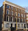 Monumentaal pand met gepleisterde benedenverdieping en bakstenen verdiepingen met hardstenen cordonbanden. Kroonlijst met klossen