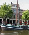 Pand onder dwars zadeldak en met gepleisterde lijstgevel. Bordes met stoephek, gesneden deur, waarboven gesneden kalf; rechts een poort, eveneens met gesneden kalf. Smalle diepliggende vensters met hardstenen dorpels en late schuiframen. Houten kroonlijst, met in het fries triglyphen en metopen