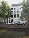Hoog herenhuis met lage bovenverdieping en eenvoudige gepleisterde lijstgevel. De deur heeft een gesneden omlijsting met touwornament en een gesneden kalf