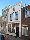 Pand met gepleisterde gevel onder rechte kroonlijst. Houten winkelpui. Gesneden deurkalf